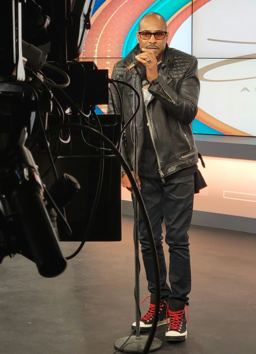 Aaron Skyy performing live on a TV studio set in a leather jacket and red-laced sneakers