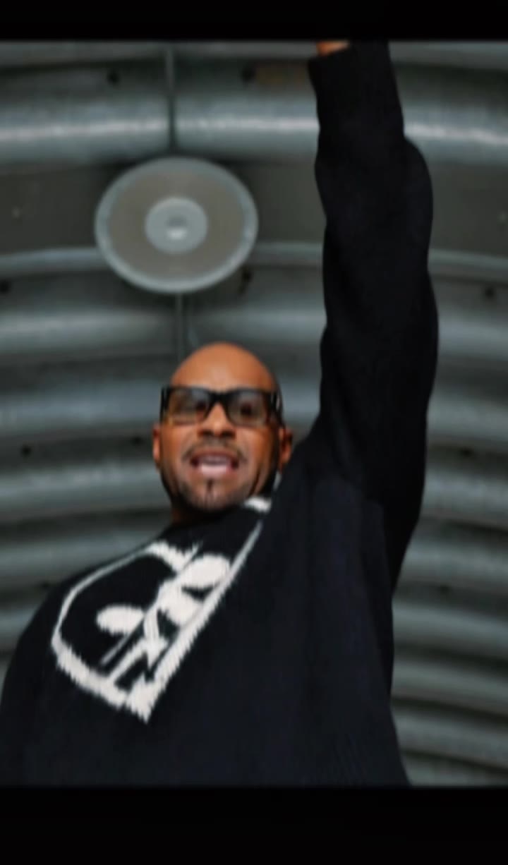 Aaron Skyy raising his fist in a corrugated tunnel, heart sweater, vertical promo